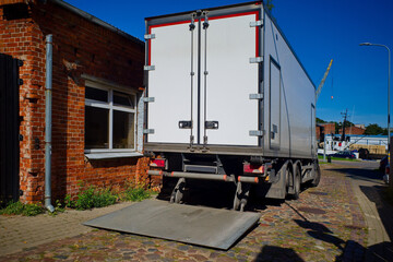 Refrigerated truck unloading at a warehouse with open tail lift on a sunny day.