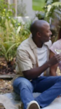 Vertical video: Arriving backyard, diverse couple toasting wine, eating grapes, checking smartphone