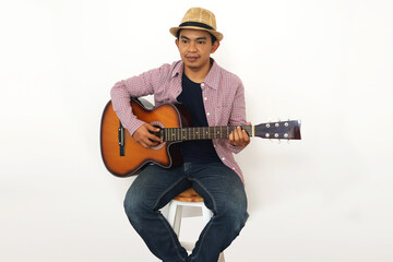Obraz premium Young Asian man in brown cowboy hat and checkered shirt holding acoustic guitar against white background