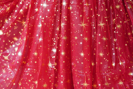 A close-up of shimmering red tulle fabric decorated with golden star patterns
