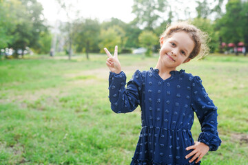 A smiling young girl wearing a navy embroidered dress poses outdoors with a playful peace sign