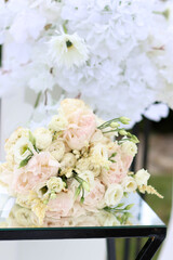 Pastel wedding bouquet of roses and lisianthus placed on mirrored table with white floral background.