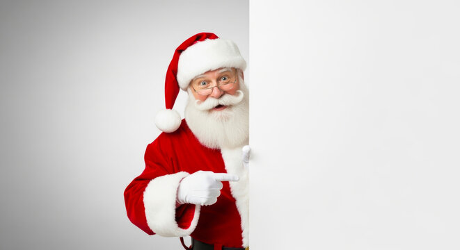Jolly santa claus peeking around a white blank board with a friendly smile and pointing finger