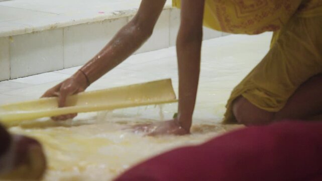Young temple priest sitting in flowing milk and pushing it away by hand with bamboo bark