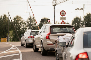 Line of cars stopped at railway crossing barrier with traffic lights and visible road signs,...