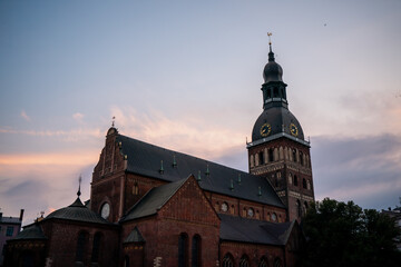 Fototapeta premium Beautiful cathedral building with clock tower and red brick walls against soft evening sky, symbolizing European history, spiritual heritage, and timeless architectural traditions