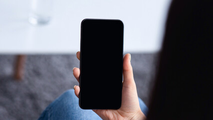 Technology for communication, surfing on internet, chat in social networks and be safe at home. Young lady holds phone with empty screen, in living room interior with table with credit card and glass