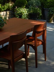 Fototapeta premium A cozy outdoor dining space showcases a wooden table surrounded by two stylish chairs amidst lush greenery