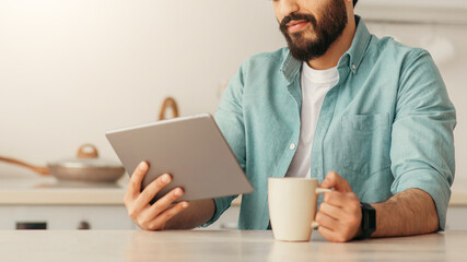 Leisure time. Young arab man reading news on digital tablet or surfing internet and enjoying...
