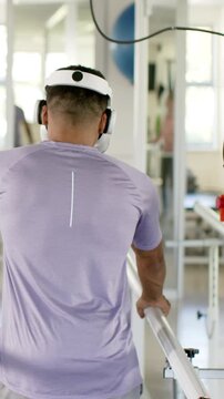 Gripping parallel bars man practicing balance in rehab gym with headset and exercise ball