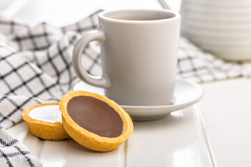 Sweet chocolate tartelettes and coffee cup on white table.