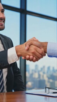 vertical. Two businessmen shaking hands at office desk with city view through window. Agreement and partnership concept. Design for poster, banner, wallpaper, header