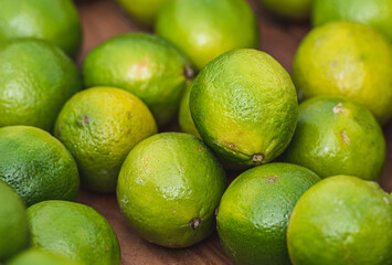 Fresh green limes piled together in a close-up shot, showcasing their smooth, glossy skin and vibrant color. The citrus fruits rest on a wooden surface, emphasizing their natural freshness and organic
