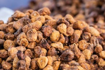 A close-up image of a large pile of dried figs, showcasing their textured, wrinkled skins and golden-brown tones. The natural lighting emphasizes the organic detail and earthy color of the figs