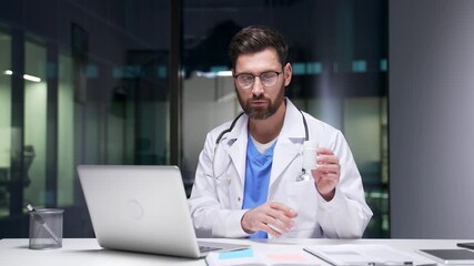 Confident doctor in white coat talking on video call using laptop sitting in hospital office. Medical worker physician communicates remotely showing medicine, has online consultation with patient