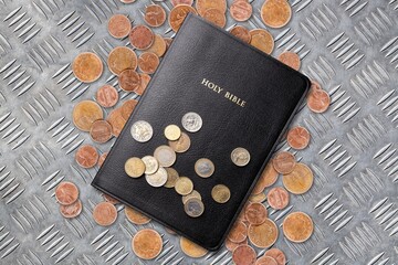 Stack of coins and Holly Bible book