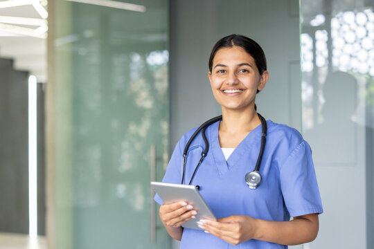 Smiling nurse holding digital tablet in hospital corridor