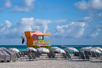 Colorful lifeguard tower with rows of white beach chairs and umbrellas on South Beach, Miami Beach, Florida, USA, under blue sky and clouds