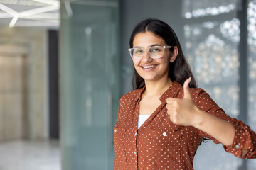 Young indian businesswoman showing thumbs up in modern office building