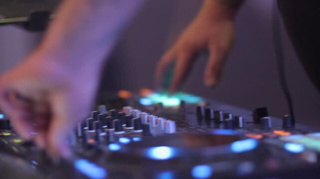 A DJ's hands skillfully operate a mixer and turntables, illuminated by colorful club lights, creating an energetic atmosphere for a night of dancing.