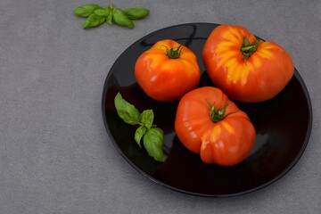 Three large tomatoes lie on a black plate, basil.