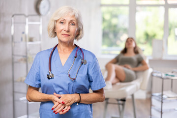 Experienced doctor with stethoscope, woman patient who is sitting behind and waiting in hospital.