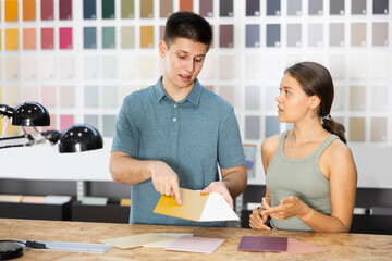Fototapeta premium In construction store, young couple near showcase with samples choose color and tone of flooring wallpaper laminate for repair. Consumables for construction and renovation overhaul