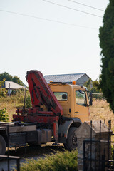 Yellow Crane Truck with Red Arm Parked Beside Roadside Vegetation in Rural Setting, Sunny Day Landscape Photography