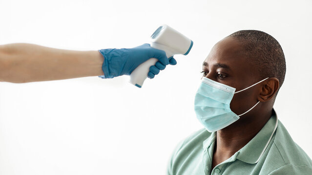 Health check, prevent covid-19 outbreak and preparation for vaccination. Doctor or nurse measures temperature with infrared thermometer in middle aged in african american patient in protective mask