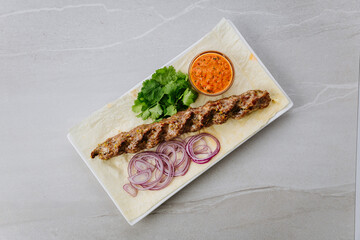 Grilled lamb lula kebab with onion, herbs, and spicy sauce on lavash bread
