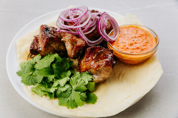 Grilled pork kebab with fresh herbs, red onion, lavash and spicy red pepper sauce