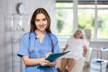 Positive young lady wearing medical coat with pen and folder in her hands standing at treatment...