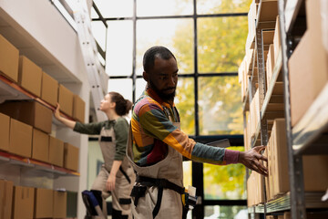 African american worker managing pallets processing in a small scale facility, organizing cargo and processing online shopping orders. Ensuring accurate small business e-shop delivery.