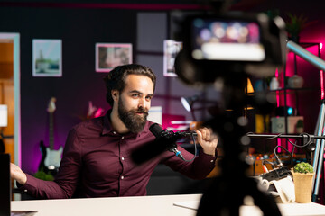 Content creator adjusting professional microphone in studio before starting recording video for social media. Influencer in rgb lit studio preparing gear for vlog shooting