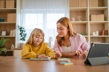 Mother helping daughter with homework, using tablet for online learning