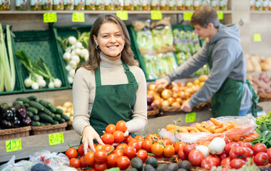 Female supermarket employee selling ripe tomatoes in the produce department