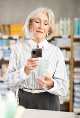 Mature woman in summer clothes scans code on package of cream to check the expiration date
