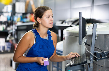 Fototapeta premium Experienced young woman seller using technical computer and mixing machine in hardware store