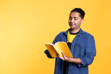 Indian male model reading a book to have fun and enjoy characters, standing with lecture against...