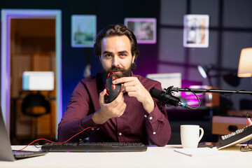 Influencer promoting wired gaming mouse from sponsor to audience in home studio. Content creator...