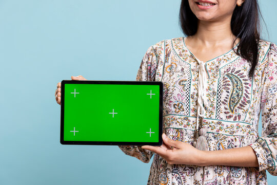 Confident woman presenting green screen on mobile gadget, standing against studio background. Cheerful indian person holding copy space chroma key smartphone used for advertising brands.