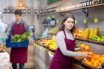 Female seller working in supermarket and lays out fresh oranges on counter