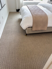 Corner view of bed with beige blanket and bright window