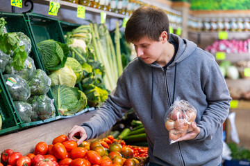 Young guy shopper in casual clothes chooses tomatoes in vegetable shop