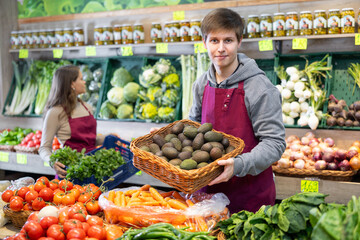 Portrait of male grocery store seller with basket of ripe kiwis in her hands
