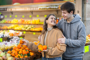 Couple of young woman and young guy choose tangerines in vegetable shop