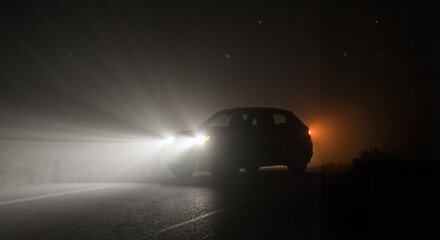 Obraz premium Car headlights illuminating road in foggy night scenery 