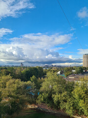 Obraz premium A scenic view of a city skyline surrounded by lush green trees under a bright blue sky with fluffy clouds. 
