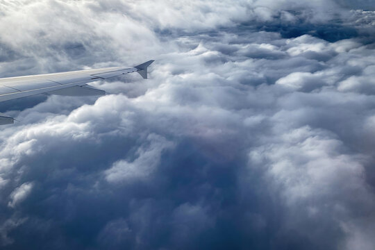 View from a passenger airplane window showing the wing and thick layers of clouds with soft light breaking through from above - Powered by Adobe