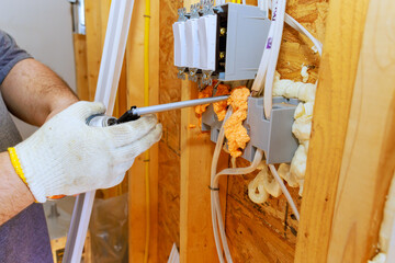 An electrician installs wiring outlets while sealing gaps with spray foam insulation in new home...